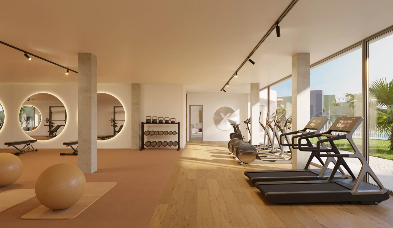 Et fuldt udstyret fitnesscenter med store vinduer med udsigt over haverne og poolområdet.